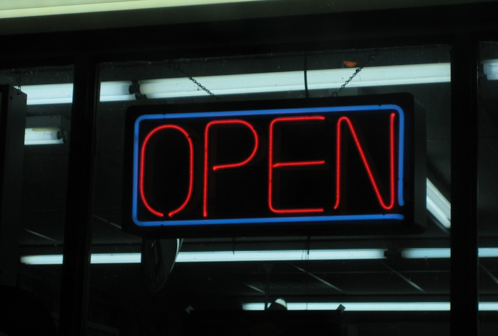 Blue-bordered red neon OPEN sign hanging in a shop window
